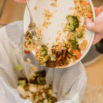 manos humanas vertiendo restos de comida en un cubo de basura